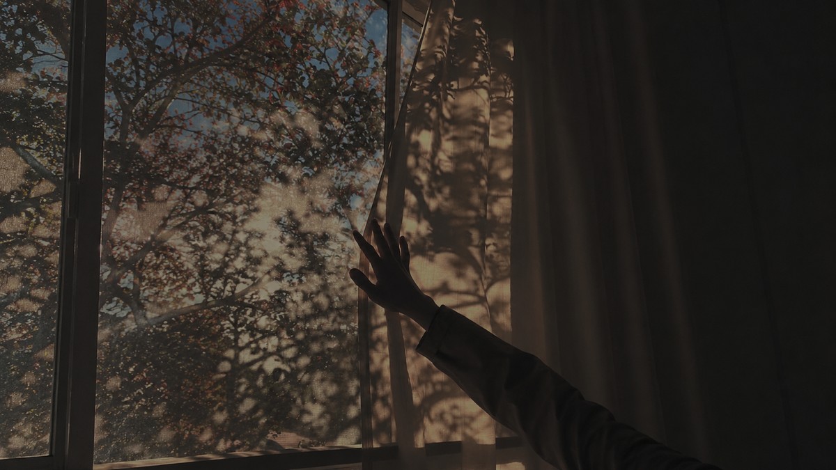 Hand touching a curtain by a window, representing a new perspective opening up