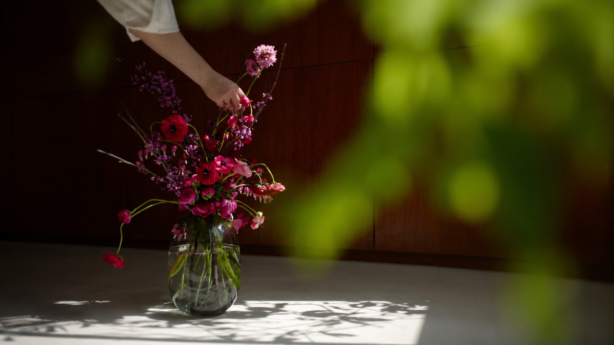 Person arranging fresh flowers in warm sunlight, representing quiet growth happening out of view